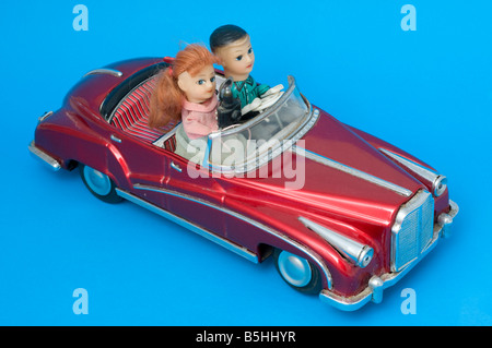 Pressed metal novelty toy battery powered car with driver sitting beside a woman photographer with camera and flash. Stock Photo