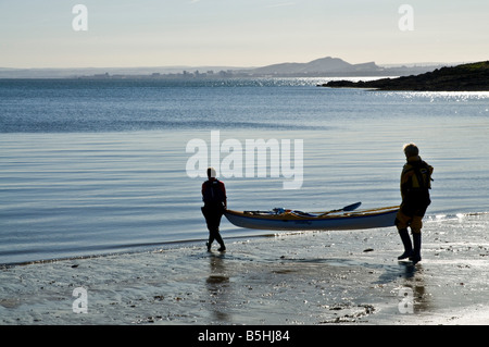 dh Couple Kayak canoes WATERSPORT KAYAKING UK SCOTLAND Two woman on beach carrying canoe to waters edge sea sport 2 people Stock Photo