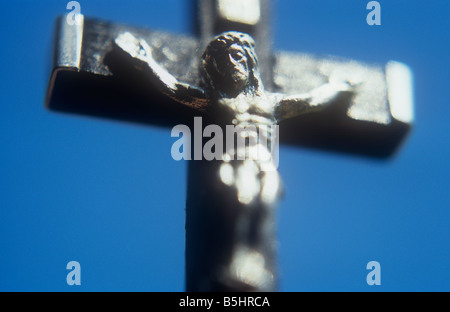Silver model of Jesus Christ hanging from black wood crucifix with silver caps against clear blue sky Stock Photo