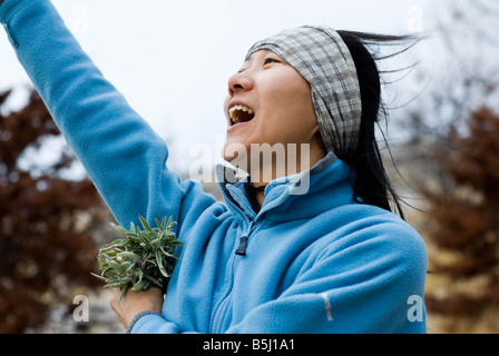 young female from profile happily extending one arm up and holding a bunch of fresh sage in the other hand. Stock Photo