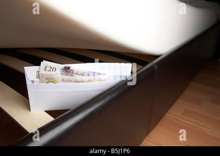 wad of 20 and 10 pounds sterling bank of england cash in an envelope stuffed under the mattress of a bed Stock Photo