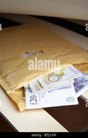 wad of 20 and 10 pounds sterling bank of england cash in an envelope stuffed under the mattress of a bed Stock Photo