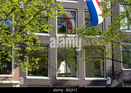 Amsterdam. House on a canal in the Jordaan with Dutch national flag and a model sailing-boat on the windowsill. Springtime. Stock Photo