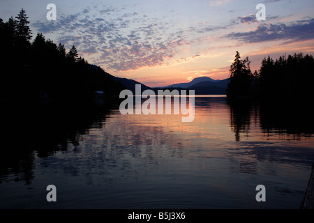 Dramatic sunset at Ruby Lake near Vancouver BC with coastal mountains in background and reflections in lake in July Stock Photo