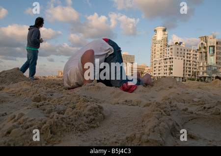 Young man burying their head in the sand during humorous event in Jerusalem Beach in Tel Aviv  Israel Stock Photo