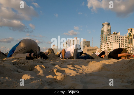 Young people burying their head in the sand during humorous event in Jerusalem Beach in Tel Aviv  Israel Stock Photo
