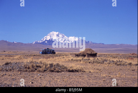 Local bus driving across the altiplano near a rustic hut, Mt Huayna Potosi in background, Bolivia Stock Photo