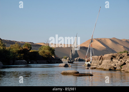 Felucca traditional boats sailing along the Nile river and the First Cataract with the Western Desert in background in Aswan Southern Egypt Stock Photo
