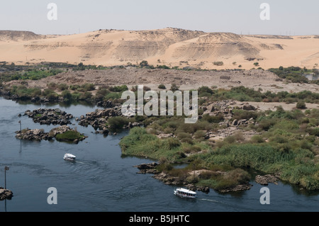 View of tour boats boating along the Nile river and the First Cataract with the Western Desert in background in Aswan Southern Egypt Stock Photo