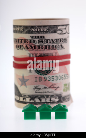 three green houses on front of a wad of 50 usa dollar bank notes cash tied up in a roll with elastic band Stock Photo