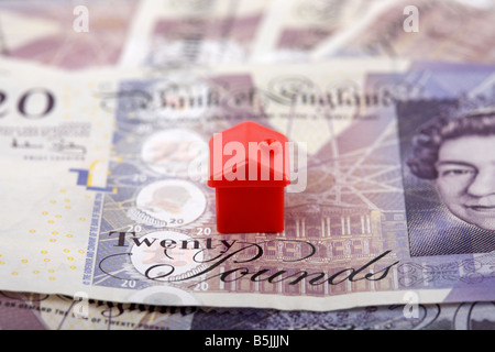 one red house on top of a pile of 20 pounds sterling bank notes cash Stock Photo