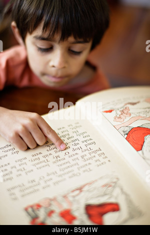 Six year old boy points to words in book as he learns to read Stock Photo