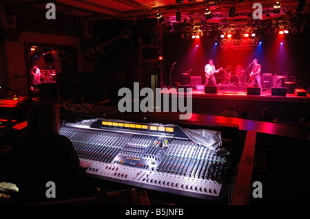 A mixer monitors the soundboard at a music hall with band performing on stage. Stock Photo