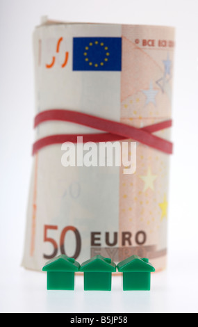 three green houses on front of a wad of 50 euro bank notes cash tied up in a roll with elastic band Stock Photo