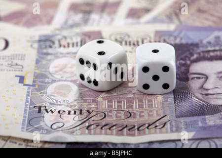 two dice on top of a pile of 20 pounds sterling bank notes cash Stock Photo