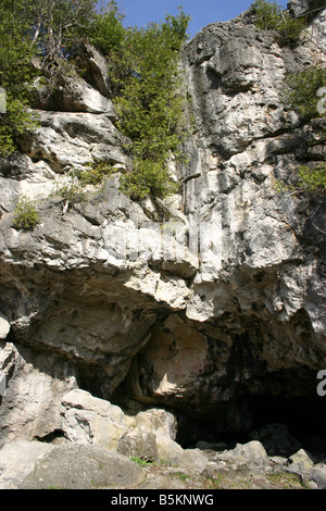 A limestone cave mouth, midway up a cliff, about ten feet above ground level. Stock Photo
