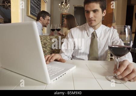 Man working with a laptop while holding a glass of wine. Stock Photo