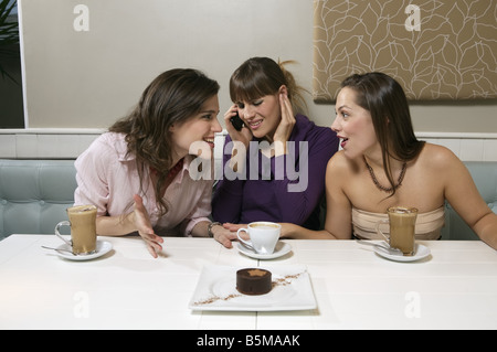 Three women enjoying their coffee with one talking on the cell phone. Stock Photo