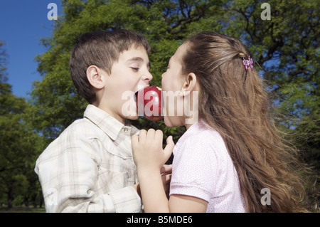 A boy and a girl biting the same apple Stock Photo