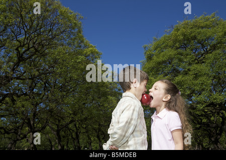 A boy and a girl biting the same apple Stock Photo