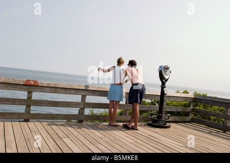 Young couple on the boardwalk at the beach, with the young woman pointing Stock Photo