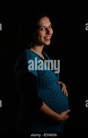 Portrait on a black background of a pregnant woman n her mid 30s enjoying her bump Stock Photo