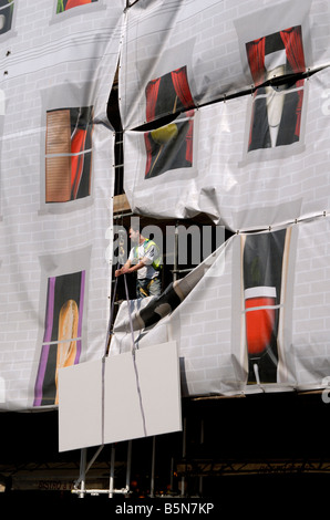 Construction worker guiding steel panel surrounded by custom scaffold sheeting printed with pub and restauraunt graphics, London Stock Photo