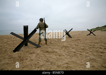 Actor dressed as an D-Day  American soldier on Utah Beach Normandy France standing next to  a 'Hedgehog' tank trap. Stock Photo