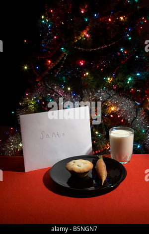 childs letter to santa left out on christmas eve with mince pie carrot and glass of milk in front of christmas tree Stock Photo