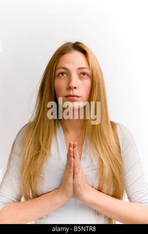 Angelic innocent looking young attractive pretty blonde haired woman with her hands pressed together in prayer, UK Stock Photo