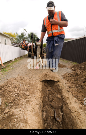 Man talking on walkie-talkie, giving instructions to young man on ditch witch, while it drills a hole for underground water pipe Stock Photo