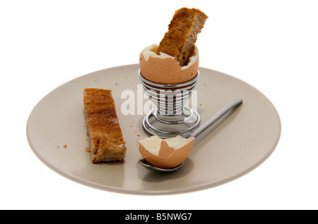 Empty Boiled egg sitting in egg cup on side plate with top cut off and a piece of toasted bread sticking out the top Stock Photo