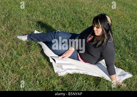 A young woman with highlighted hair reading a book on the school campus Stock Photo