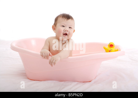 Baby boy sitting in a pink baby tub with a yellow rubber duck, laughing Stock Photo