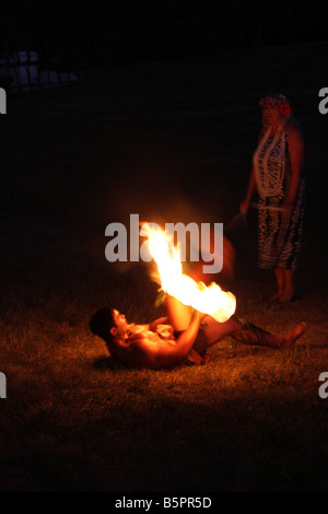 Hawaiian Fire Dancer performing at night laying down twirling a fire stick and is in a dangerous position Stock Photo