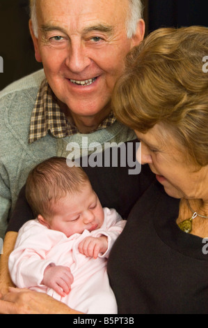 Vertical studio portrait of proud grandparents cuddling their newborn baby granddaughter. Stock Photo