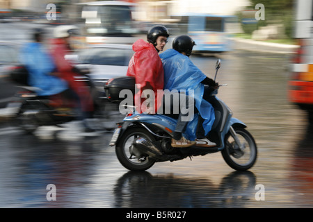 group young tourists riding rental hire scooters mopeds in rain in rome italy Stock Photo