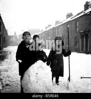 A nostalgic image of Kids making a Snowman, in the Street in the 1950s, in Northampton, England Stock Photo