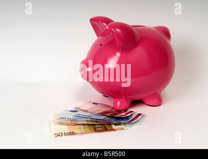 side profile of a pink piggy bank with a pile of Euro bank notes sitting in front of it. Stock Photo