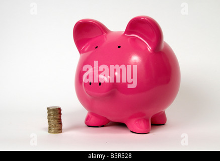 half side profile of a pink piggy bank with a pile or stack of pound coins sitting in front of it on a white back ground. Stock Photo