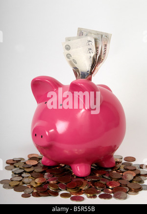 side profile of a pink piggy bank sitting on a pile of coins with British bank notes coming out the top of it. Stock Photo