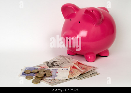 side profile of a pink piggy bank sitting in front of a pile of british bank notes and coins Stock Photo