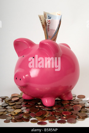 half profile view of a pink piggy bank sitting on a pile of coins with euro bank notes sticking out the top of it Stock Photo