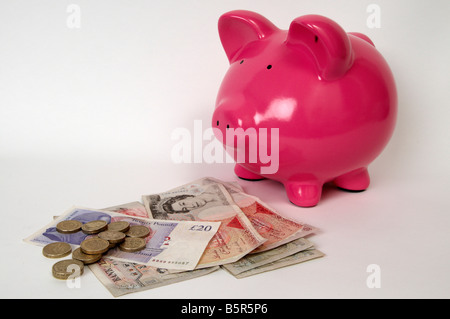 half side profile of a pink piggy bank sitting in front of a pile of British bank notes and pound coins. Stock Photo