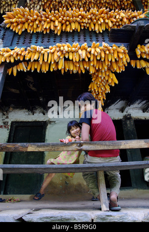 A boy and a girl sits on a bench under the corn hung out to dry in the small village of Katmati, Tamakoshi Valley, Nepal. Stock Photo