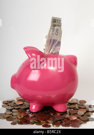 side profile of a pink piggy bank sitting on a pile of coins with British bank notes sticking out of it. Stock Photo