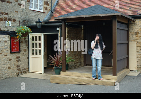 woman smoking outside due to smoking ban in pubs, The Red Lion, Cranford St Andrew, Northamptonshire, England, UK Stock Photo