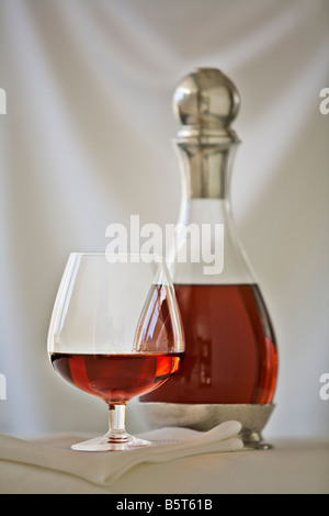 snifter of brandy with a decanter against a white fabric draped background Stock Photo