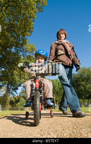 Small boy on bike with his mother walking beside him Stock Photo