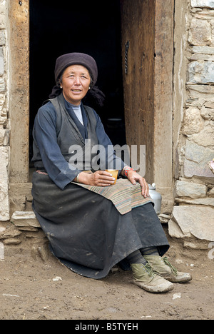 Friendly Tibetan woman sitting at the door to her home and sipping locally brewed beverage. Tibet Stock Photo